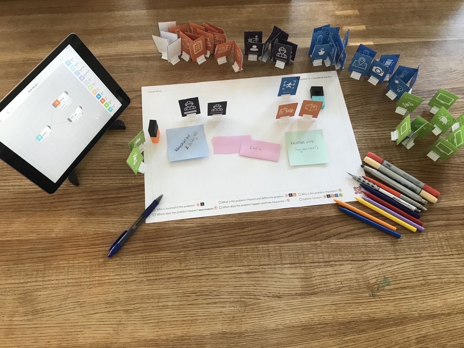 The Karakuri IoT toolkit on a table: standing paper tokens in four colours around a paper canvas, small sensor blocks and a tablet
