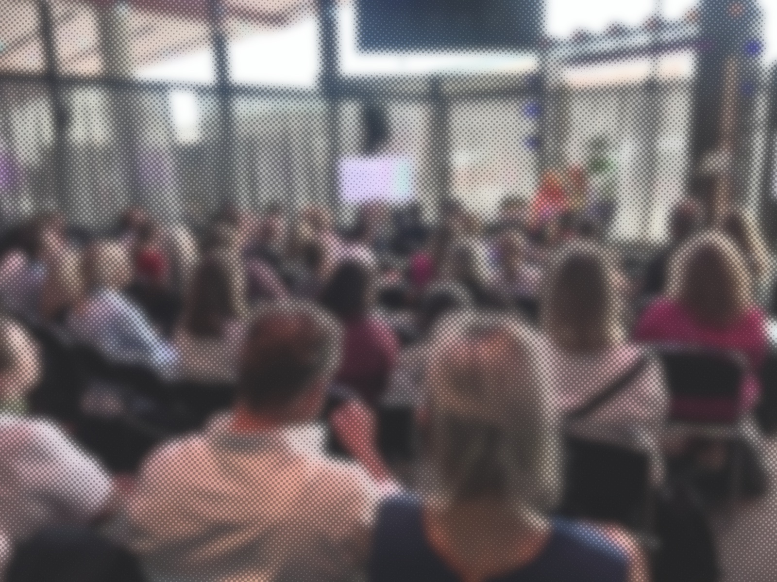Blurred halftone photo of a full room seen from behind the audience, with a stage, two speakers and a screen showing the cover of Att leda tillsammans
